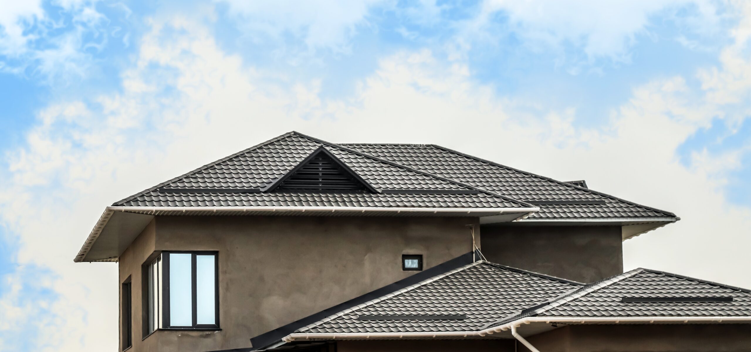 Modern house with gray tiled roof under blue sky.